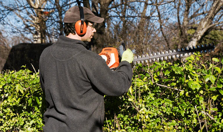 Homeowner trimming shrubs while wearing safety glasses and protective gear