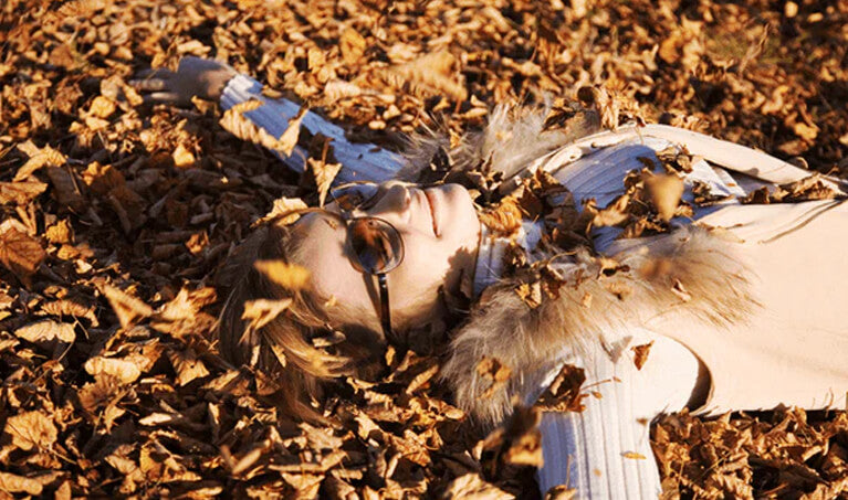 Woman wearing sunglasses while laying in a pile of leaves
