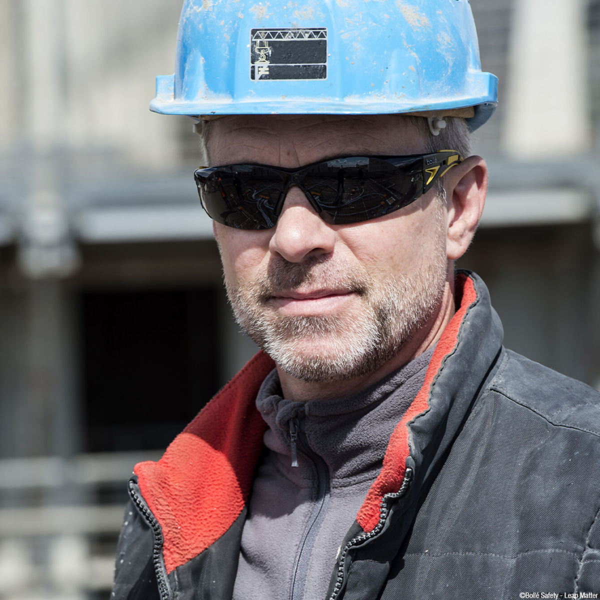 Bolle 40244 Rush Plus Safety Glasses Yellow/Black Temples Smoke Platinum Anti-Fog Lens worn by worker with a blue hard hat