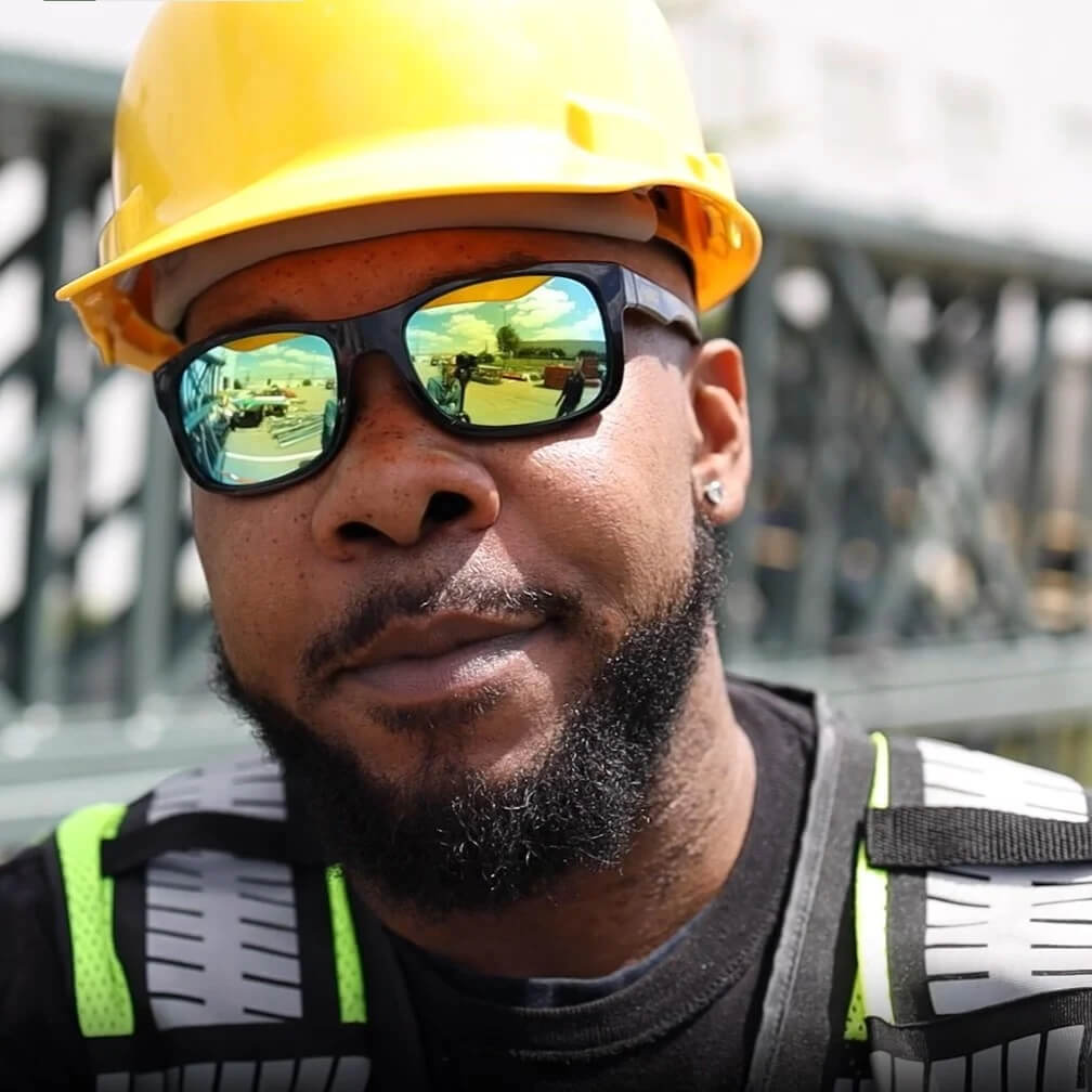 DEWALT DPG107-YD Supervisor Safety Glasses - Black Frame - Yellow Mirror Lens worn by construction worker wearing a yellow hard hat
