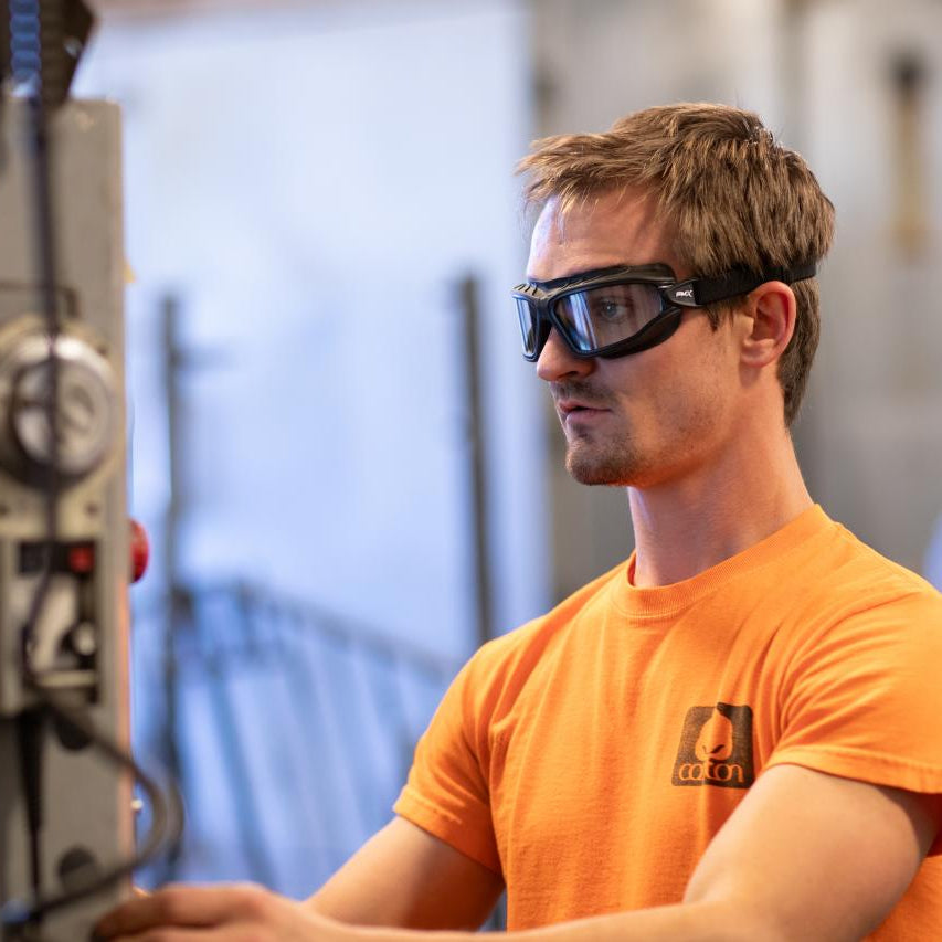 Worker wearing Pyramex Torser Safety Goggles and an orange shirt while operating machinery