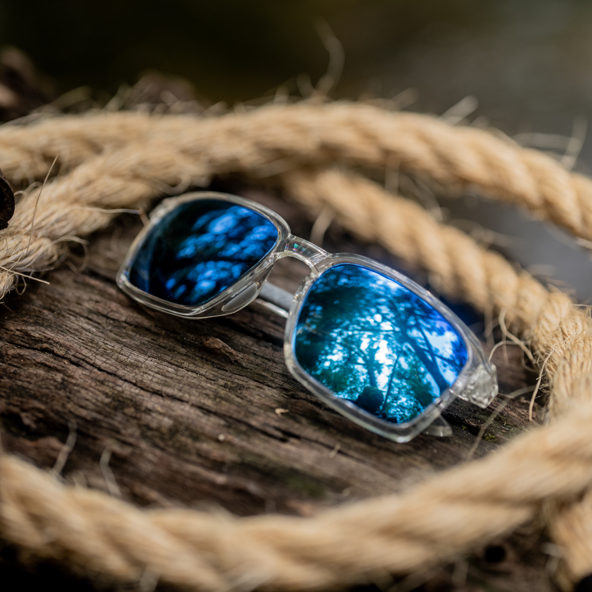Wiley X Alfa Sunglasses with blue lenses and clear frames on a wooden surface with a rope