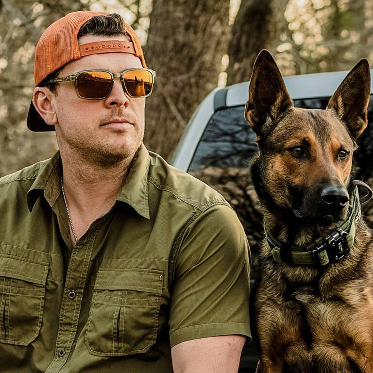 Hunter wearing Wiley X ALFA Safety Glasses with Bronze Mirror Lenses while sitting on a truck's tailgate with his dog